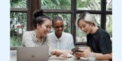 Three women sat together at a table collaborating on a project smiling at a great idea. 